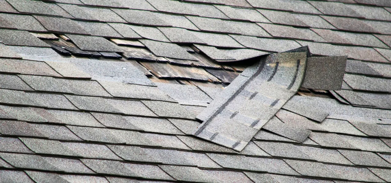 Damaged and missing asphalt shingles on a worn roof