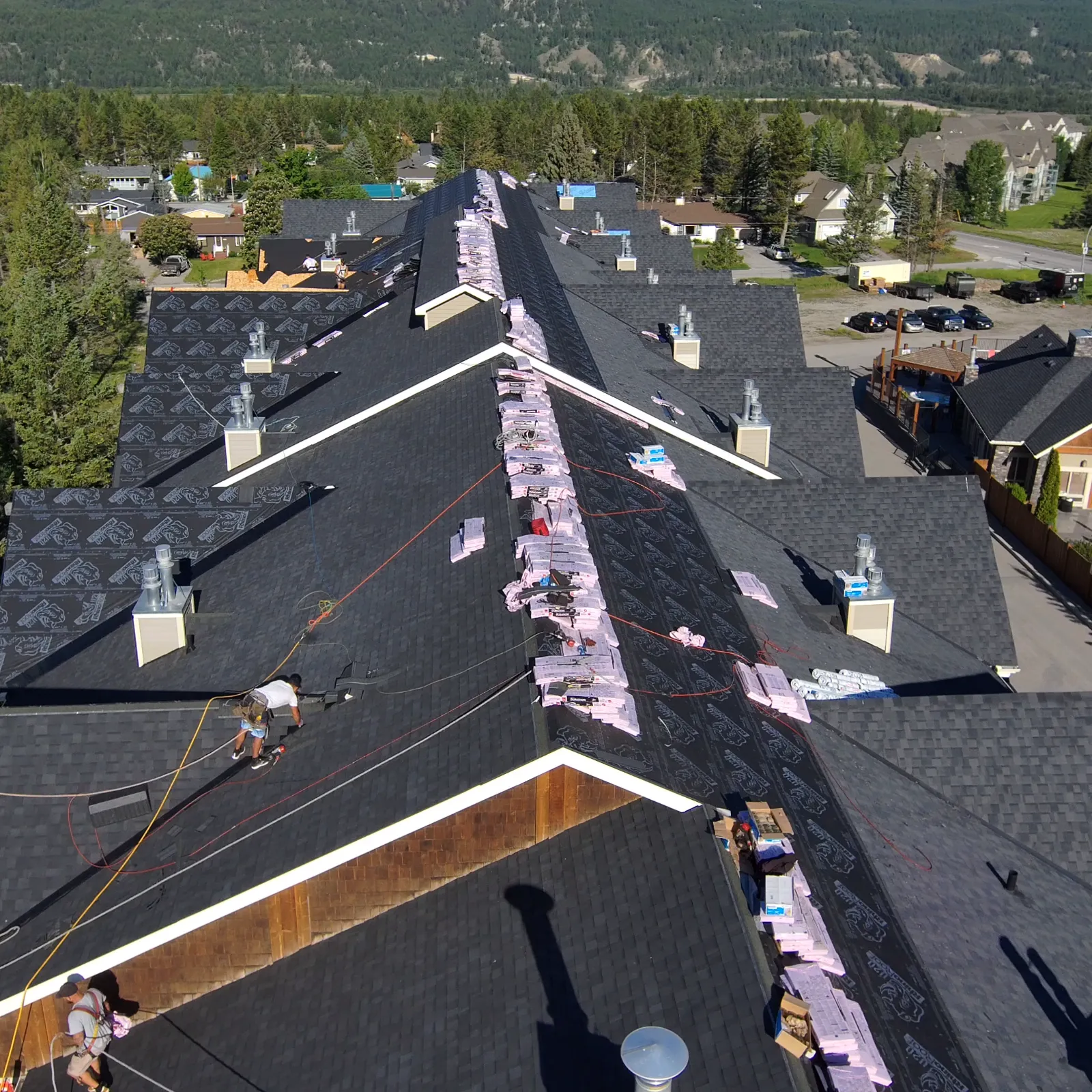 Drone view of a multi-building condo complex mid re-roof, with bundles staged along the roof peaks