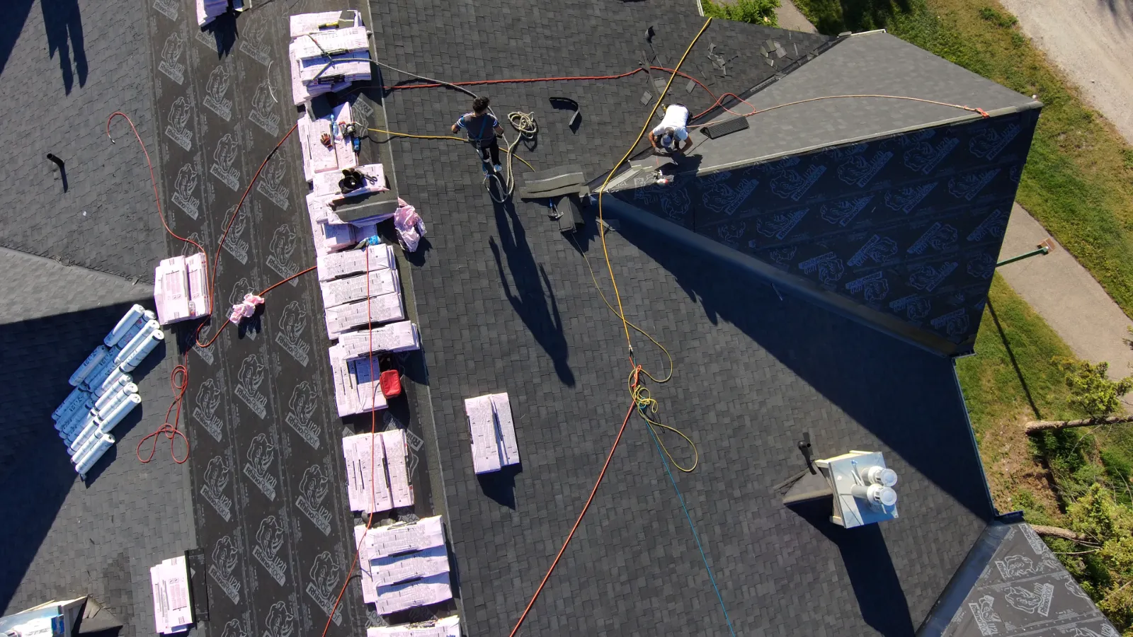 Overhead drone view of a harnessed roofing crew working among shingle bundles on a strata condo roof