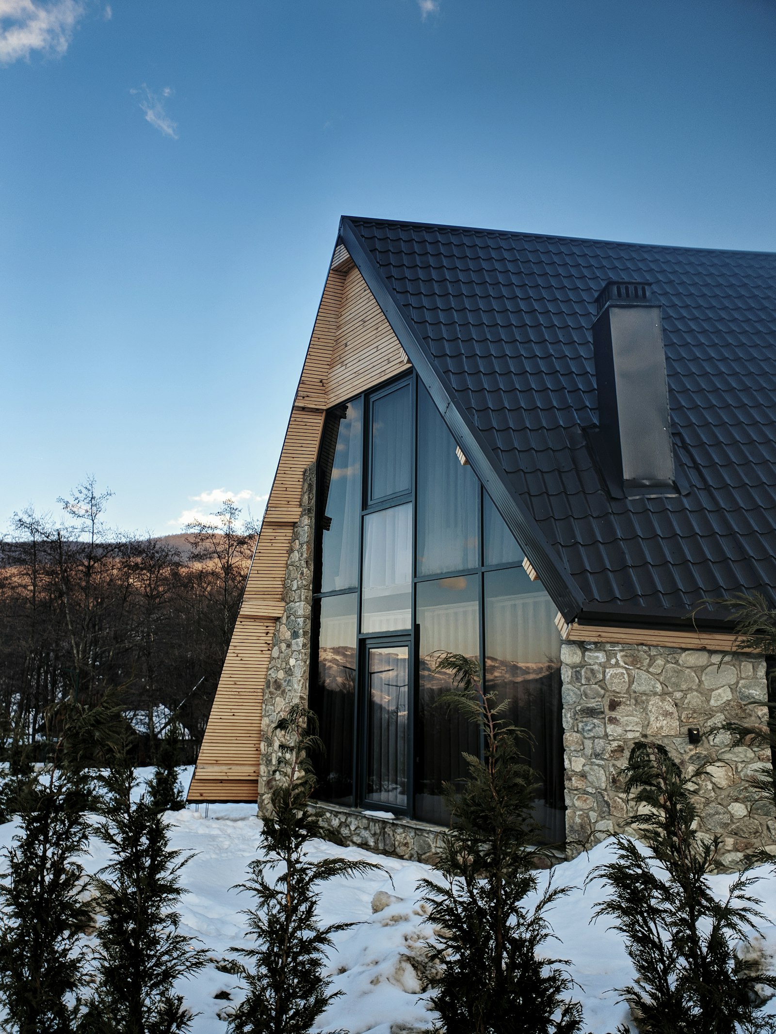 Stone A-frame cabin with tall glass windows in the mountains