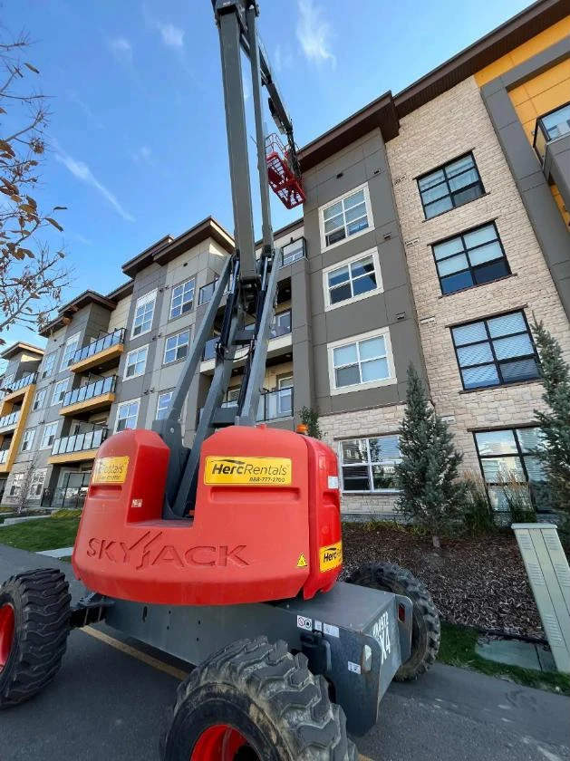 The manlift on the ground beside the condo building, boom raised to the top floor, Calgary, AB
