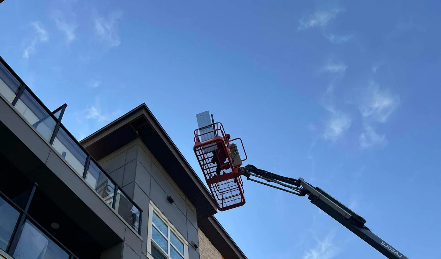 Crew working from a manlift basket at the roofline of a condo building, Calgary, AB