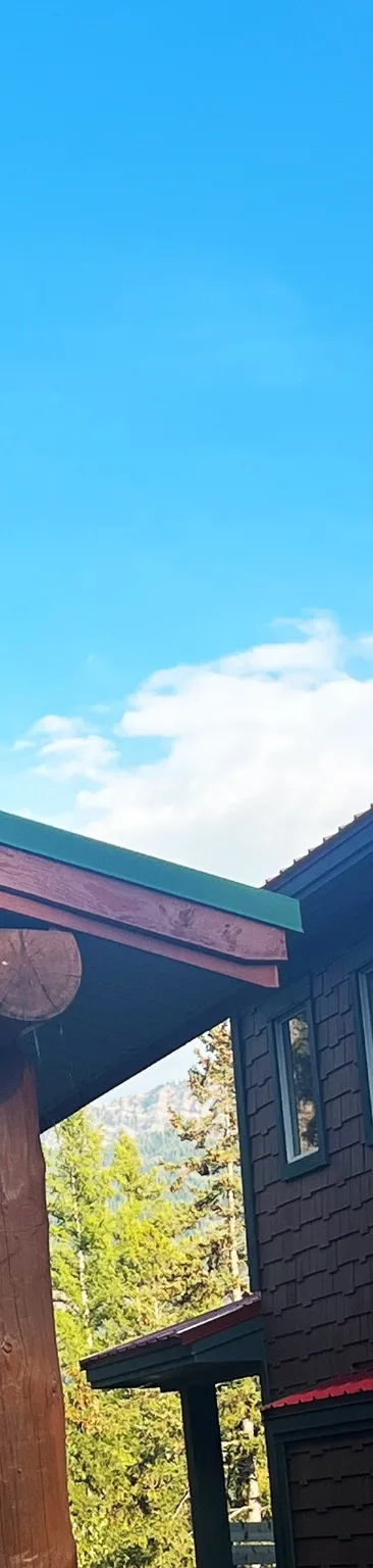 Finished green metal trim on the roofline beside a log post, Fernie, BC